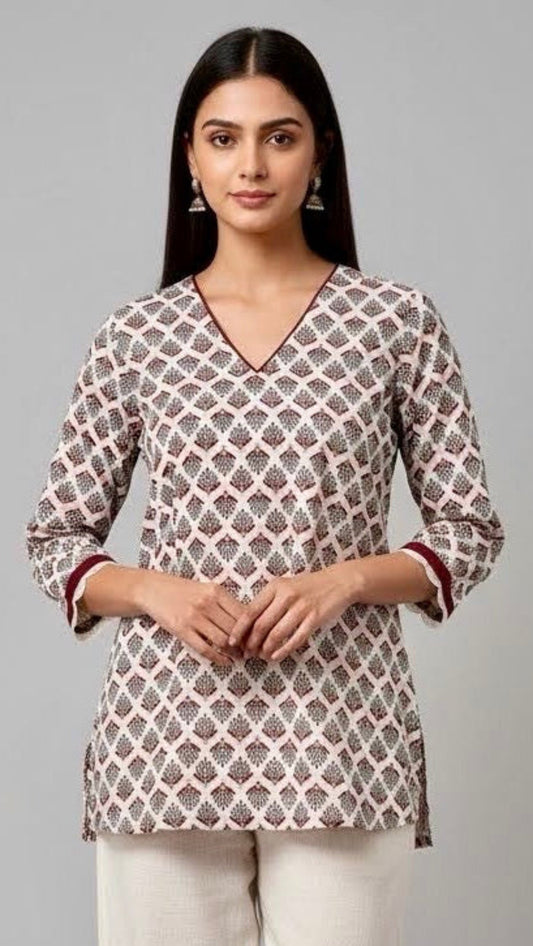 Woman wearing a patterned top and white pants on a gray background