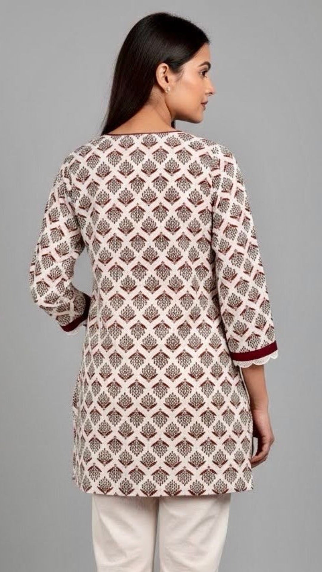 Woman wearing a patterned kurta with white pants on a gray background
