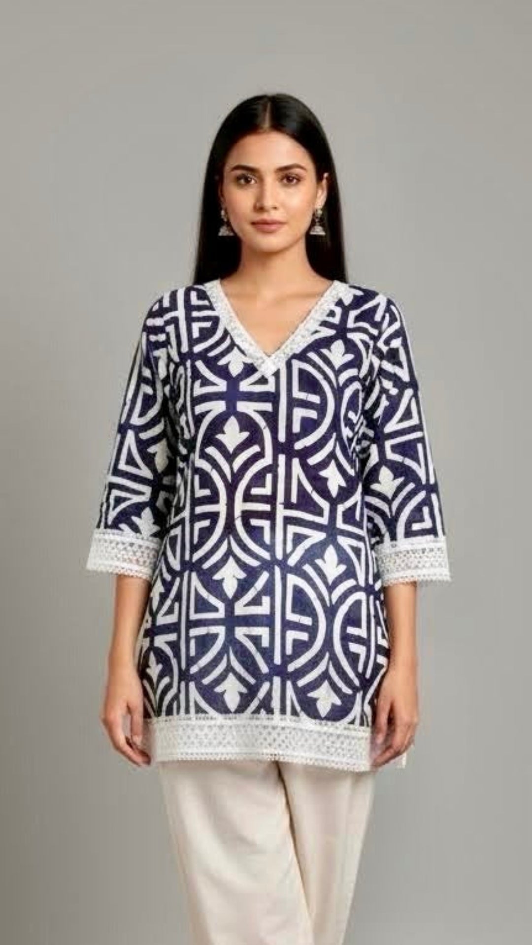 Woman wearing a blue and white patterned top with white pants on a gray background
