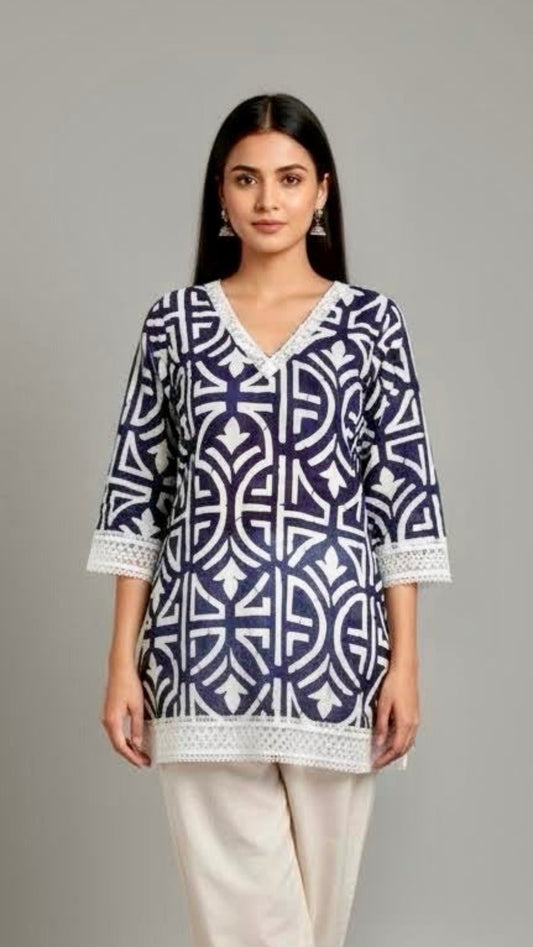 Woman wearing a blue and white patterned top with white pants on a gray background