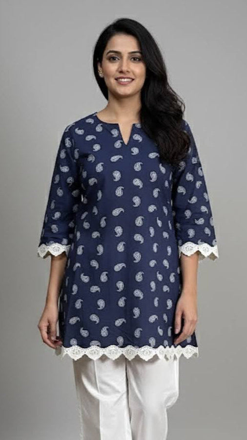 Woman wearing a navy blue patterned top and white pants on a gray background