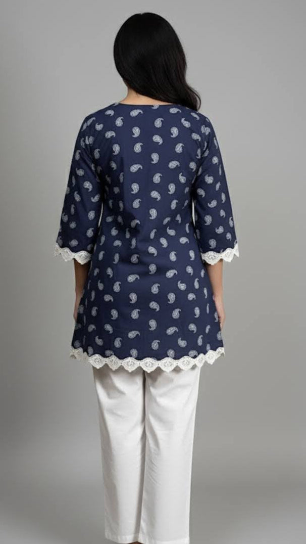 Woman wearing a navy blue patterned top with white trim and white pants on a gray background