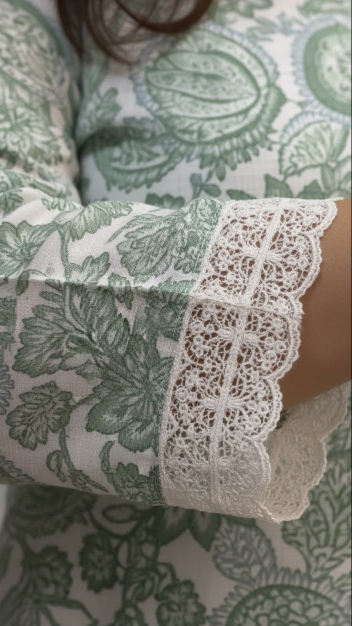 Close-up of a sleeve with lace trim on a green and white patterned fabric.