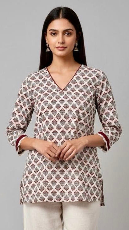Woman wearing a patterned top and white pants on a gray background