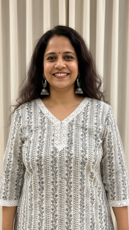 Woman wearing a patterned white and gray dress standing against a striped curtain background