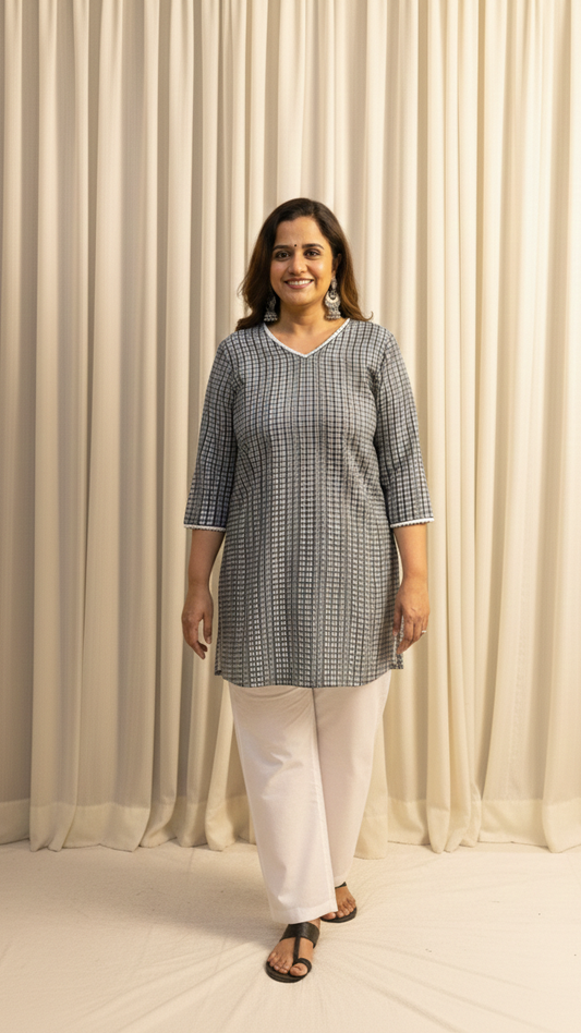 Woman wearing a checkered kurta with white pants against a beige curtain background
