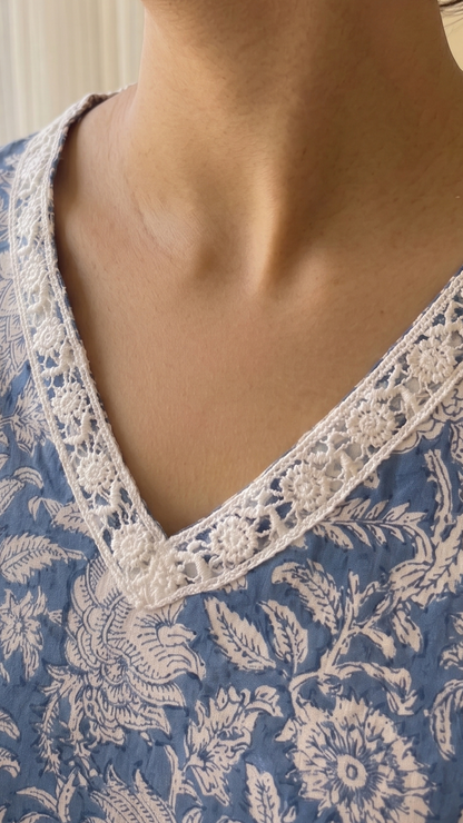 Woman wearing a blue floral top with lace trim in a softly lit room.