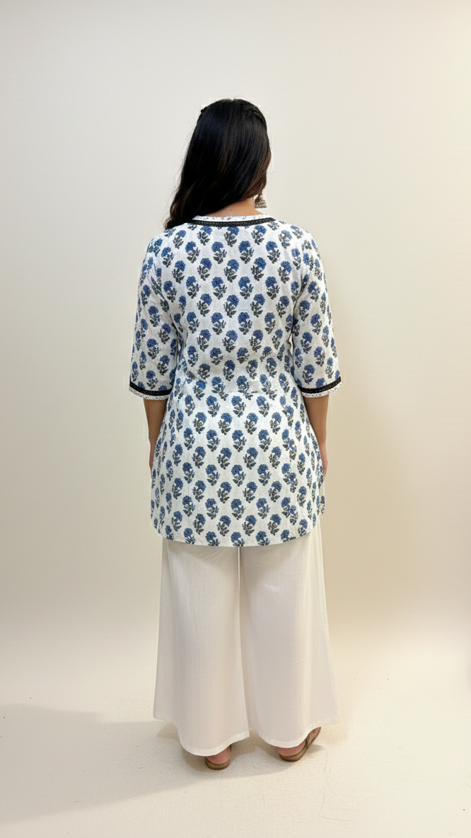 Person wearing a floral patterned top and white pants against a plain background