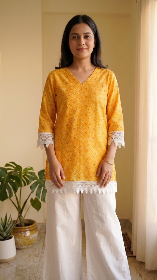 Woman wearing a yellow top with lace details and white pants in a bright room.