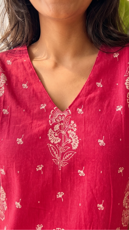Woman wearing a red floral dress indoors with a plant in the background