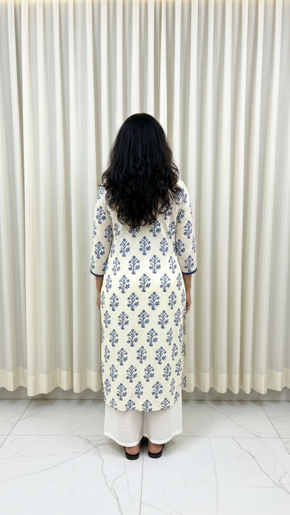 Woman wearing a floral patterned dress standing in front of a white curtain.
