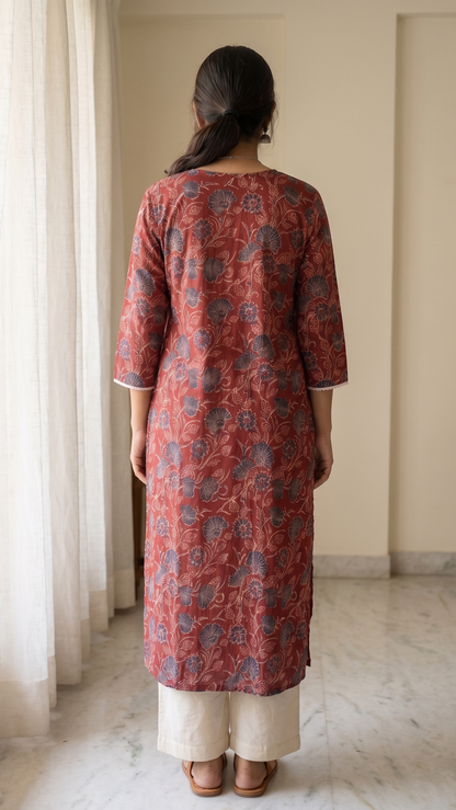 Woman wearing a red floral kurta standing in a room with light-colored walls and a window.
