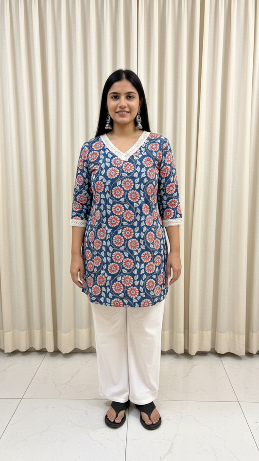 Woman wearing a blue floral top and white pants standing against a beige curtain background