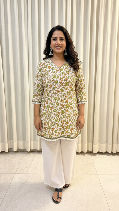 Woman wearing a floral kurta with white pants against a white curtain background