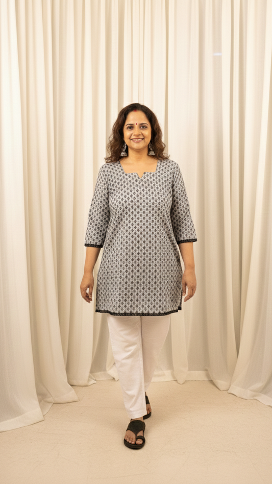Woman wearing a patterned kurta with white pants against a white curtain background