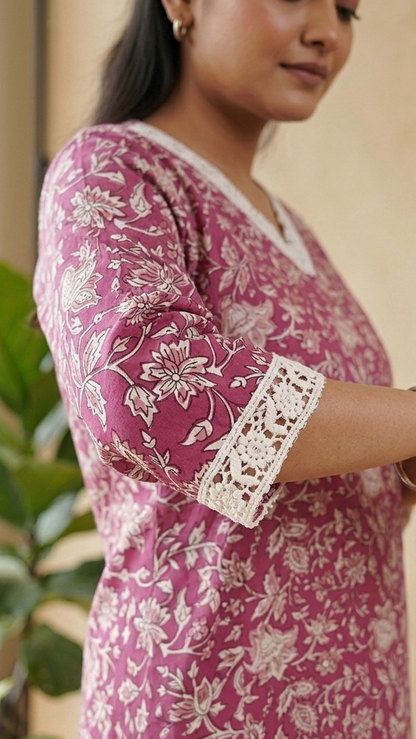 Woman wearing a pink floral dress with lace trim in an indoor setting.