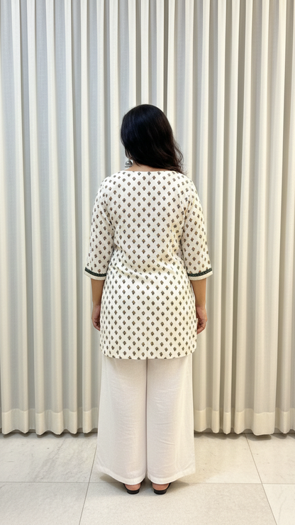 Person wearing a white polka dot top and light-colored pants standing against a striped curtain.