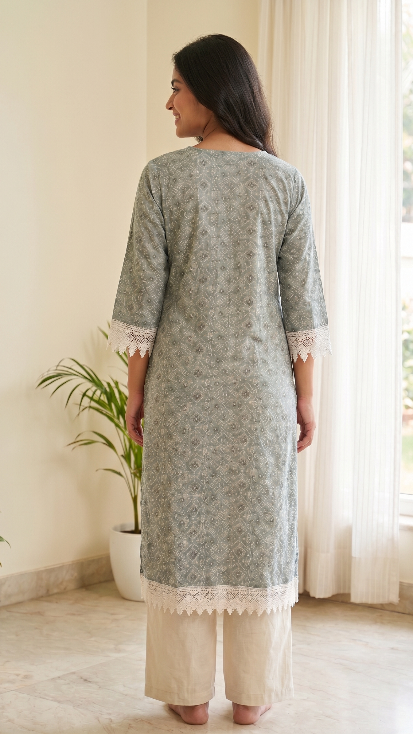 Woman wearing a gray floral kurta with white pants standing in a bright room with plants.