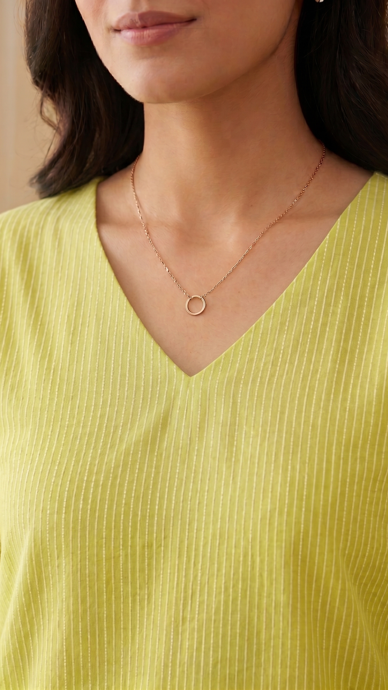 Woman wearing a green stitches kurti and a gold necklace with a circular pendant.