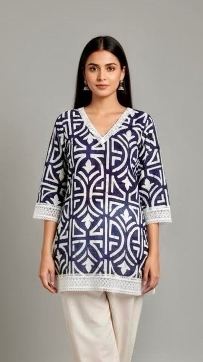 Woman wearing a blue and white patterned top with white pants on a gray background