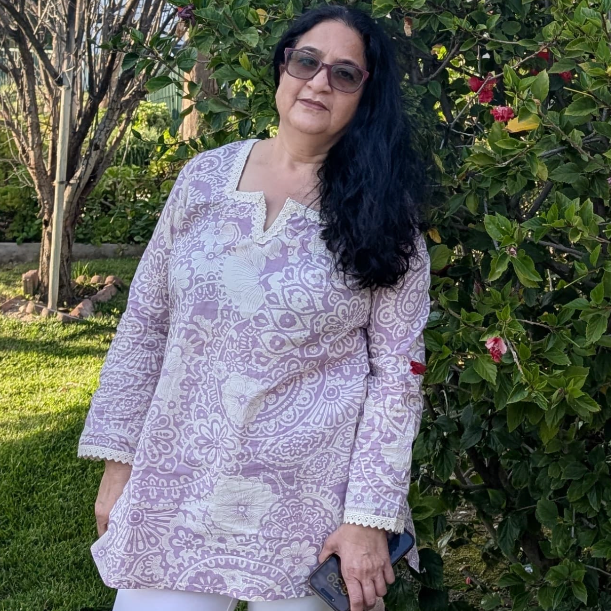 Woman standing outdoors with greenery and flowers in the background