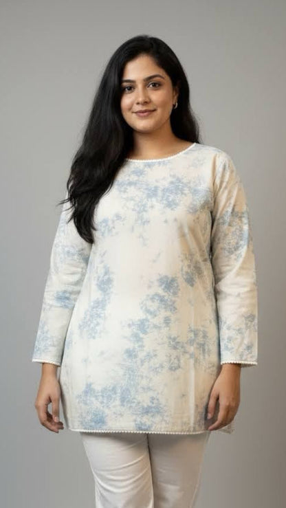 Woman wearing a floral top and white pants on a gray background