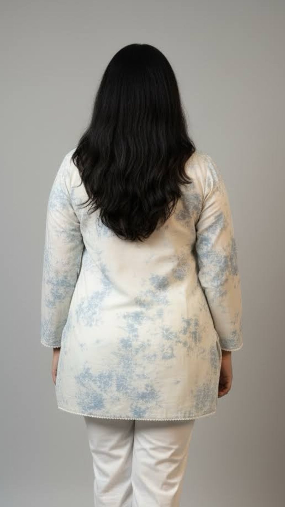Person wearing a light-colored floral top and white pants on a plain background
