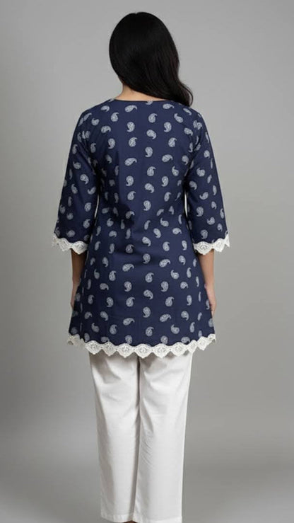 Woman wearing a navy blue patterned top with white trim and white pants on a gray background