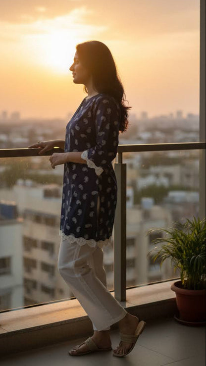 Woman standing on a balcony overlooking a cityscape at sunset.